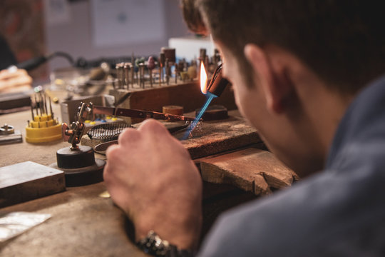 Jeweller crafting on a wooden work bench with a blowpipe
