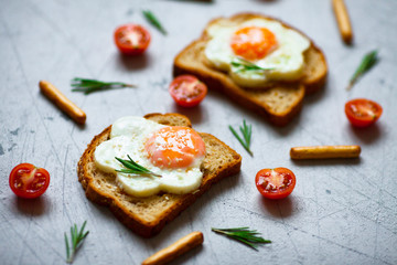 Fried eggs sandwiches with fresh tomatoes and rosemary on the tray background. Healthy breakfast or snacks. Lifestyle, diet, food styling concept. Top view. Close up. Space for a text.