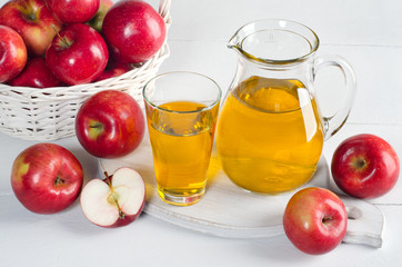 Apple juice in a decanter and a glass with apples on white table.