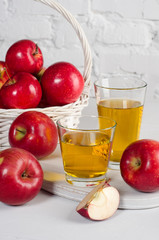 Apple juice in glasses with apples close-up on white table.