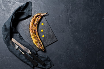 Baked bananas with honey on a black stone Board. Black background, top view, close up