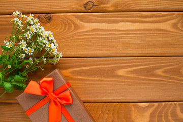 Wildflowers and gift with orange ribbon on the wooden background. Holiday and date concept.Top view. Copy space. Close up.