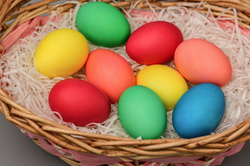 Obraz na płótnie Canvas Close - up of Easter colored eggs that lie in a wicker basket on a gray background. Horizontal photography