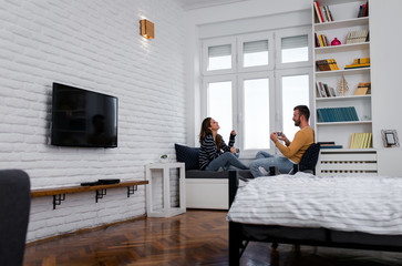 Loving couple sitting together by the window in the apartment and drinking coffee in the morning.