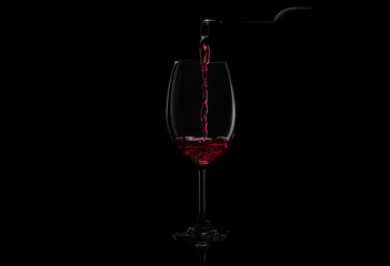 Red wine pouring in a glass from a bottle. Studio shot on black background.