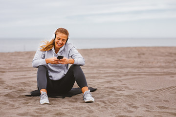 Young sports woman listens to music on the beach