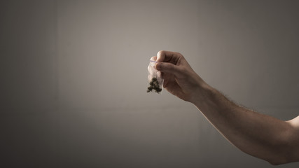 partial view of man holding pack with marijuana on grey background