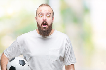 Young caucasian hipster man holding soccer football ball over isolated background scared in shock with a surprise face, afraid and excited with fear expression © Krakenimages.com