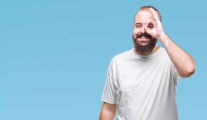 Young caucasian hipster man wearing casual t-shirt over isolated background doing ok gesture with hand smiling, eye looking through fingers with happy face.