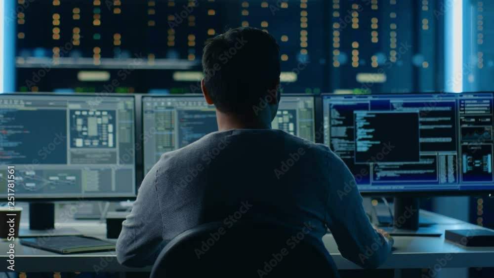 Poster IT Specialist Working on Personal Computer with Monitors Showing Coding Language Program with System Monitoring Interface. In the Background Technical Room of Data Center. Back to the Camera Shot
