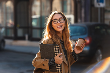 Photo of brunette woman drinking takeaway coffee while walking through city street © Drobot Dean
