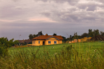 Rural  landscape with cloudy sky and red roof brick house. Hills landscape with dramatic sky as background. 