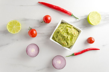 Top view of bowl with fresh made quacamole and different ingredients on marble table in the kithen