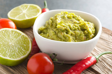 Fresh homemade guacamole with various of ingredients. Bowl with mexican salad on wooden tray