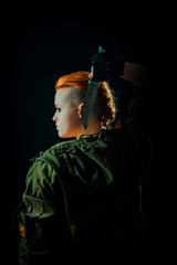 Young woman with red hair stand back in military uniform, keep a knife in hand. Vertical photo