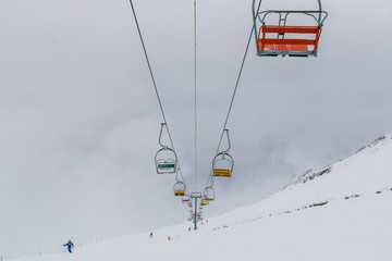 Fototapeta na wymiar Empty old lifts for two people. Dvuhkreselny ski lift in the snow and fog. Multicolored broken gondolas in Dombai, Caucasus, Karachay-Cherkessia, Russia.