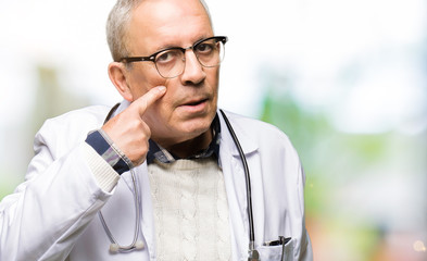 Handsome senior doctor man wearing medical coat Pointing to the eye watching you gesture, suspicious expression