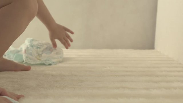 Baby sits in the diaper and plays with new fresh diapers, close-up, cotton