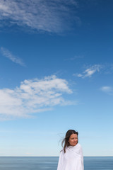 Beautiful dark hair young white european woman wrapped in white cloth sheet. In a blue sky background. Shot on Parnidis dune in Nida, Lithuania, in Curonian Spit. Sunny day with blue sky.