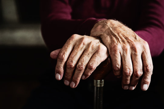 Old man hands on wooden cane. Poor health in old age.