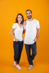 Full length photo of beautiful couple smilings while standing, isolated over yellow background - obrazy, fototapety, plakaty