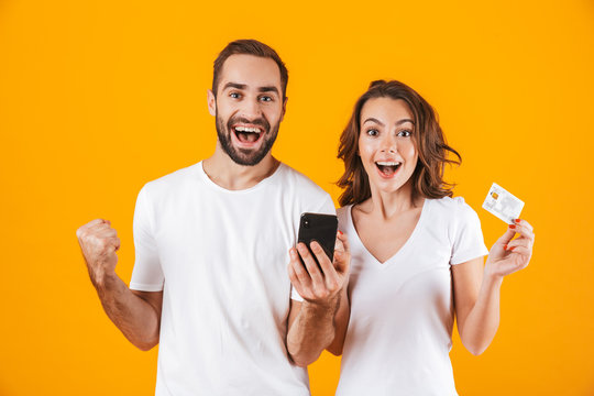 Image of positive couple man and woman using cell phone and credit card, isolated over yellow background