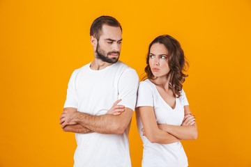 Photo of unhappy man and woman in quarrel standing back to back with arms folded, isolated over yellow background