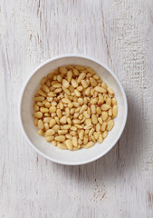 pine nuts in bowl on white wood background