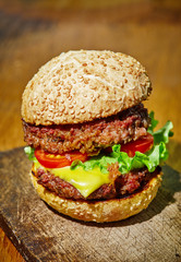 Hamburger with beef, cheese and vegetables on rustic wood background