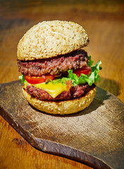 Hamburger with beef, cheese and vegetables on rustic wood background