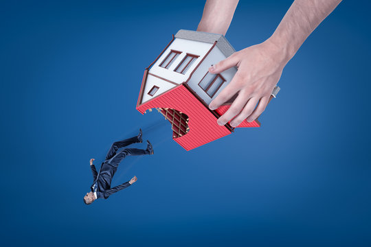 Close-up of man's hands holding house with hole in roof upside down and dropping out little businessman.