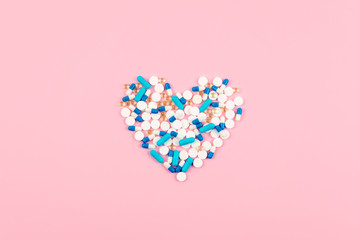 Bright blue and white pills and tablets in heart shape on pink background. Medicines, drugs, pharmacy concept. Flat lay, top view, minimal style