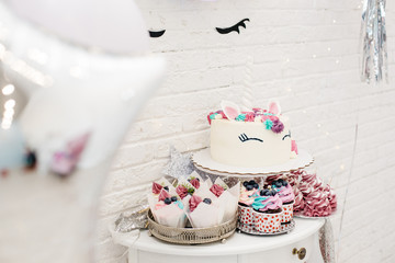 Festive decoration of the holiday in the style of a unicorn. Table with sweets and decorations made of paper, glitter and lights