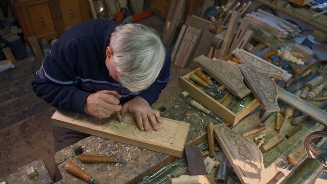 Wood carver is carving an oak plank on his table in the workshop.