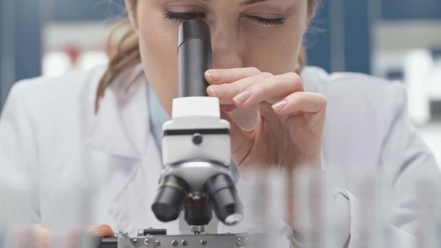 female scientist in white coat looking through microscope in laboratory