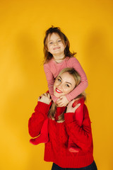 Happy little girl with her young mother on the yellow background. Daughter sitting on mom's neck. Smile