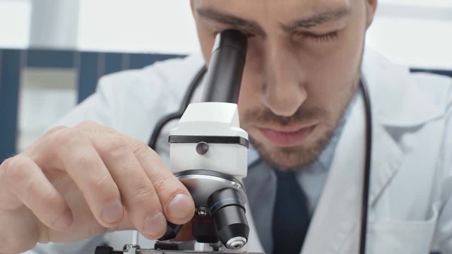 concentrated male scientist looking through microscope in laboratory