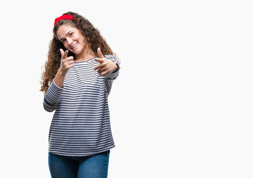 Beautiful brunette curly hair young girl wearing stripes sweater over isolated background pointing fingers to camera with happy and funny face. Good energy and vibes.