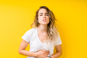 Young beautiful blonde woman over yellow background with hand on stomach because indigestion, painful illness feeling unwell. Ache concept.