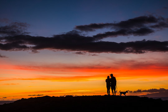 Romantic couple wioth dog enjoying and looking the sunset with red and orange coloured clouds in the sky - wanderlust and travel concept for happy people - dawn and colors background concept