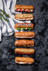 Different salty eclaires with cheese, ham, red caviar, spinach on a dark gray background