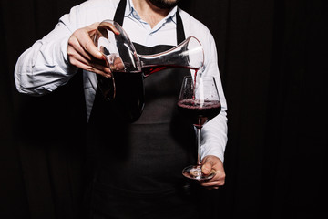 Sommelier is pouring red wine into a wineglass on a dark background