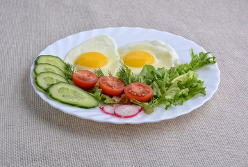 Breakfast. Fried eggs with vegetables. Sliced cucumber, tomato, green salad, radish, fresh dill and two eggs on a white plate. Rustic.