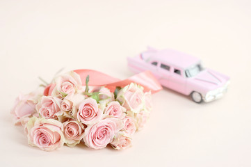 A bouquet of spray roses and a pink toy car. Free space to place text. Light background. The concept of holiday greetings.