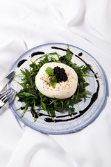 Burratta cheese with arugula and balsamic vinegar pearls on a white background