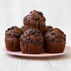 Chocolate muffins on round pink plate on white wooden table, side view. Close-up. Selective focus.
