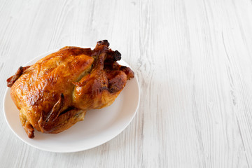 Homemade tasty rotisserie chicken on white plate over white wooden background, low angle view. Copy space.