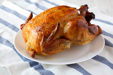 Homemade rotisserie chicken on white plate, side view. Close-up.
