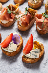 Different types of bruschetta with meat and cheese on a gray concrete background close-up