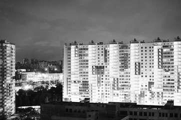 Multi-storey residential buildings with luminous windows. Night city landscape. Black and white photography.